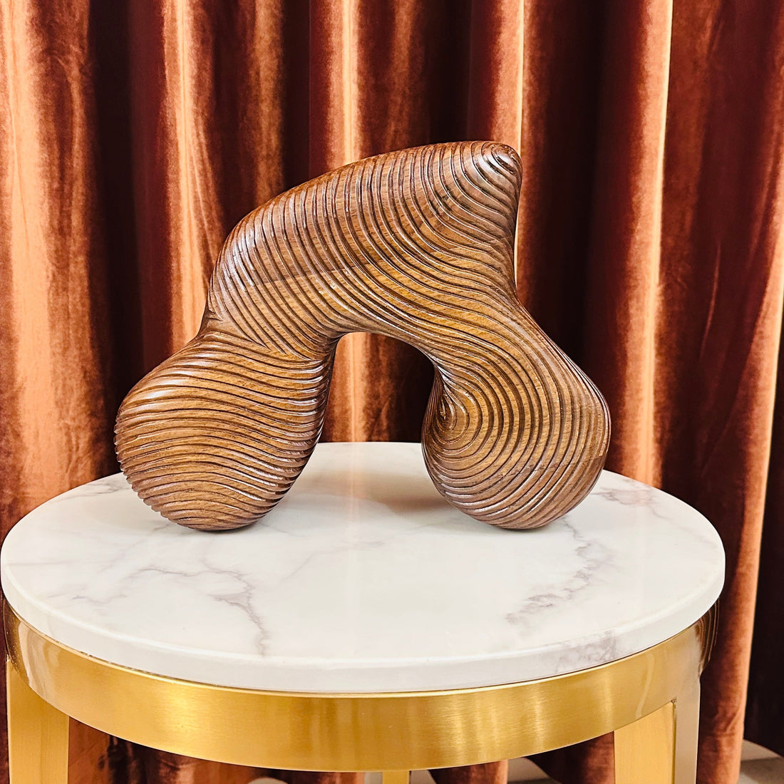 Decorative sculpture on a marble stool with gold base against a brown curtain background